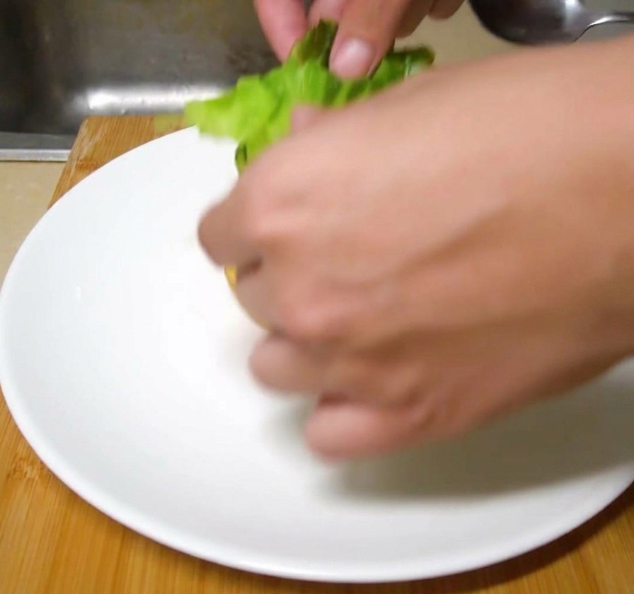 Foglie fresche di lattuga verde adagiate a mano sul panino per hamburger pronto sul piatto.