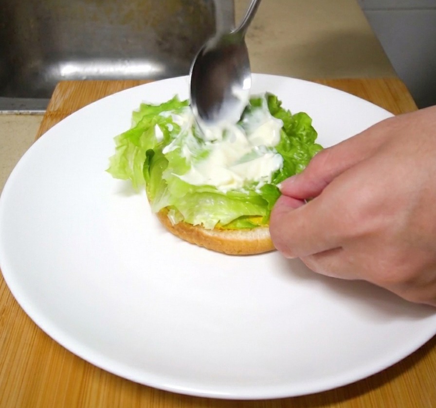 Un cucchiaio che stende un velo di maionese cremosa sopra le foglie di lattuga fresca.
