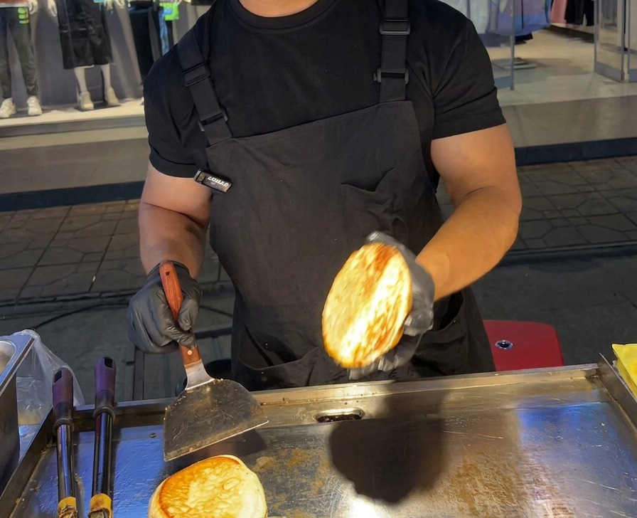 Una persona mostra la metà di un panino per hamburger perfettamente tostato e dorato sopra una piastra in acciaio inox.