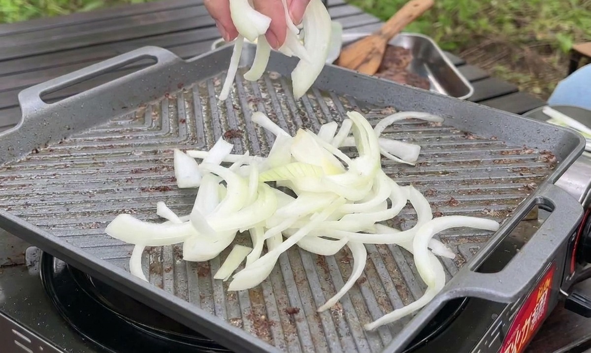 Sottili fette di cipolla bianca vengono lasciate cadere su una piastra calda per essere saltate vicino alla carne.