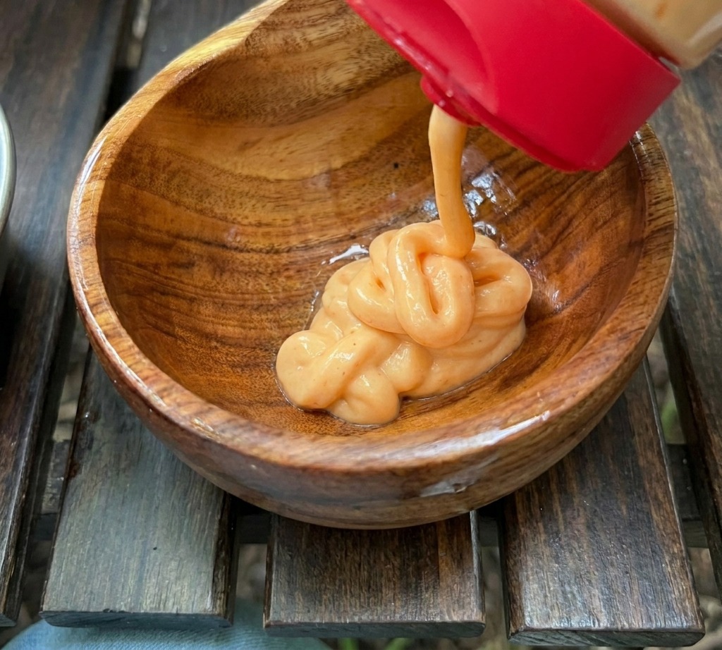 Una cremosa salsa arancione viene spremuta in una piccola ciotola di legno contenente altri ingredienti.