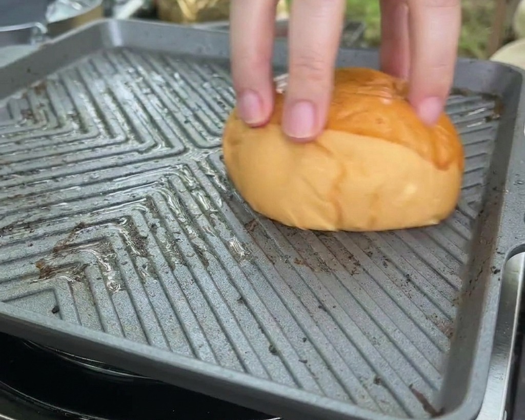 Un panino brioche viene premuto a faccia in giù su una calda piastra quadrata per tostare la parte tagliata.