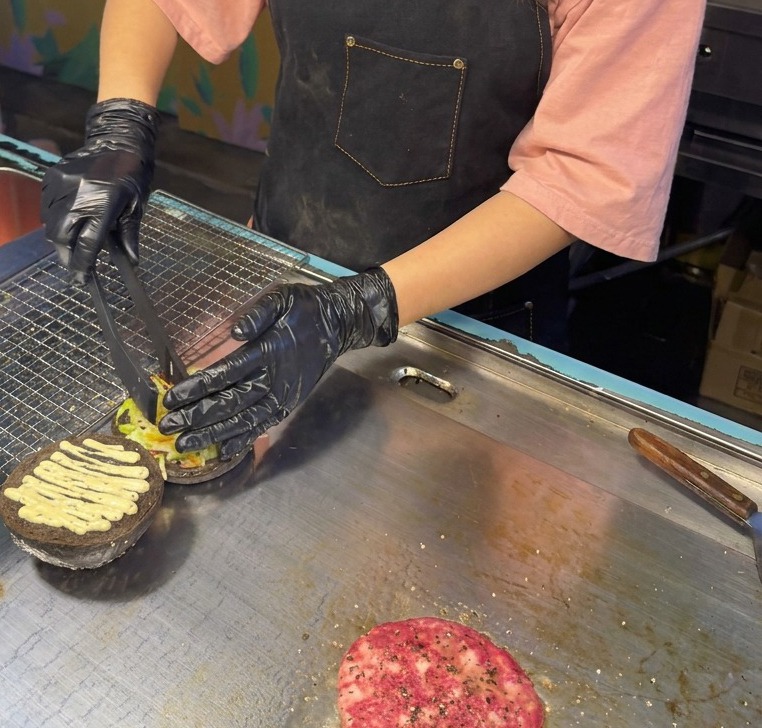 Una pinza adagia un mix di lattuga e cavolo viola tritati sulla base di un panino nero già condito con la salsa al tartufo.
