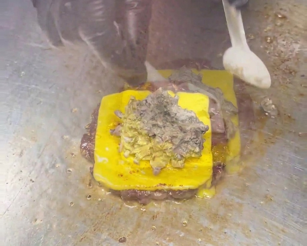 Un cucchiaio distribuisce una densa e cremosa salsa grigio-marrone ai funghi sopra un cheeseburger.