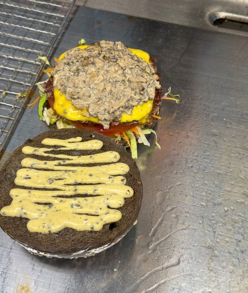 Una generosa porzione di funghi affettati e saltati riposa sopra un hamburger assemblato con formaggio e salsa.