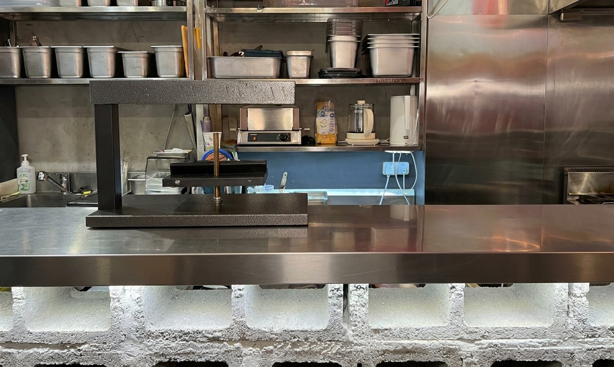Uno scaldaraclette elettrico nero pronto alluso su un bancone in acciaio inossidabile di una cucina professionale.