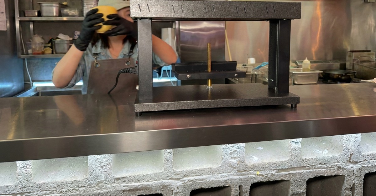 Mani con guanti che posizionano un blocco semicircolare di formaggio sulla base di una macchina per raclette.