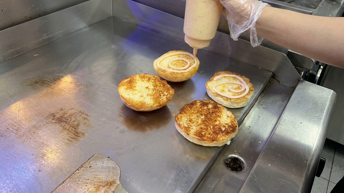 Salsa rosa cremosa applicata con un movimento circolare su un panino brioche tostato sulla piastra.
