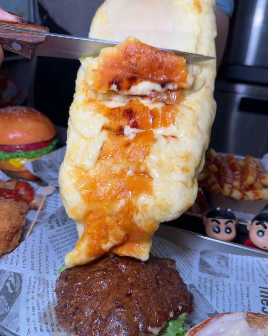 Un generoso strato di formaggio fuso e dorato che viene raschiato da una forma con un coltello sul patty di un burger.