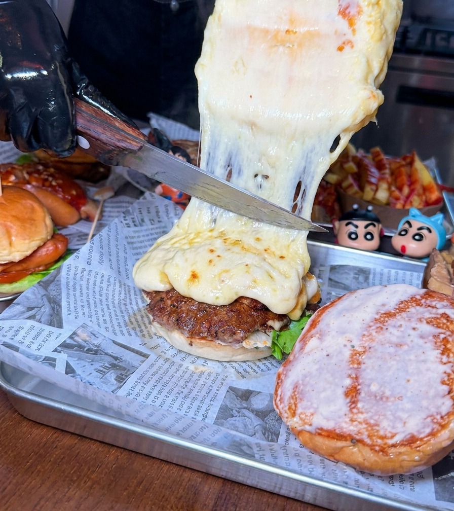 Un grande coltello che raschia uno spesso strato di formaggio fuso e bollente da una forma direttamente sul burger.