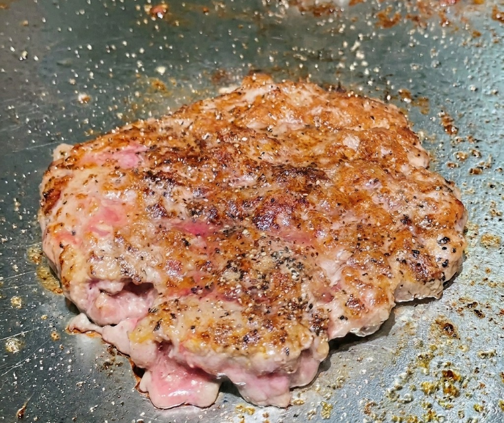 Un tortino di manzo girato sulla piastra che mostra una superficie ben rosolata, dorata e croccante.