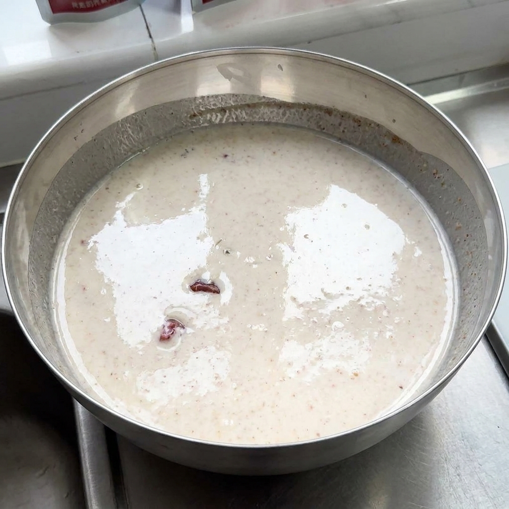 Pezzi di pollo crudo immersi in una grande ciotola di metallo piena di marinatura cremosa allo yogurt e spezie.