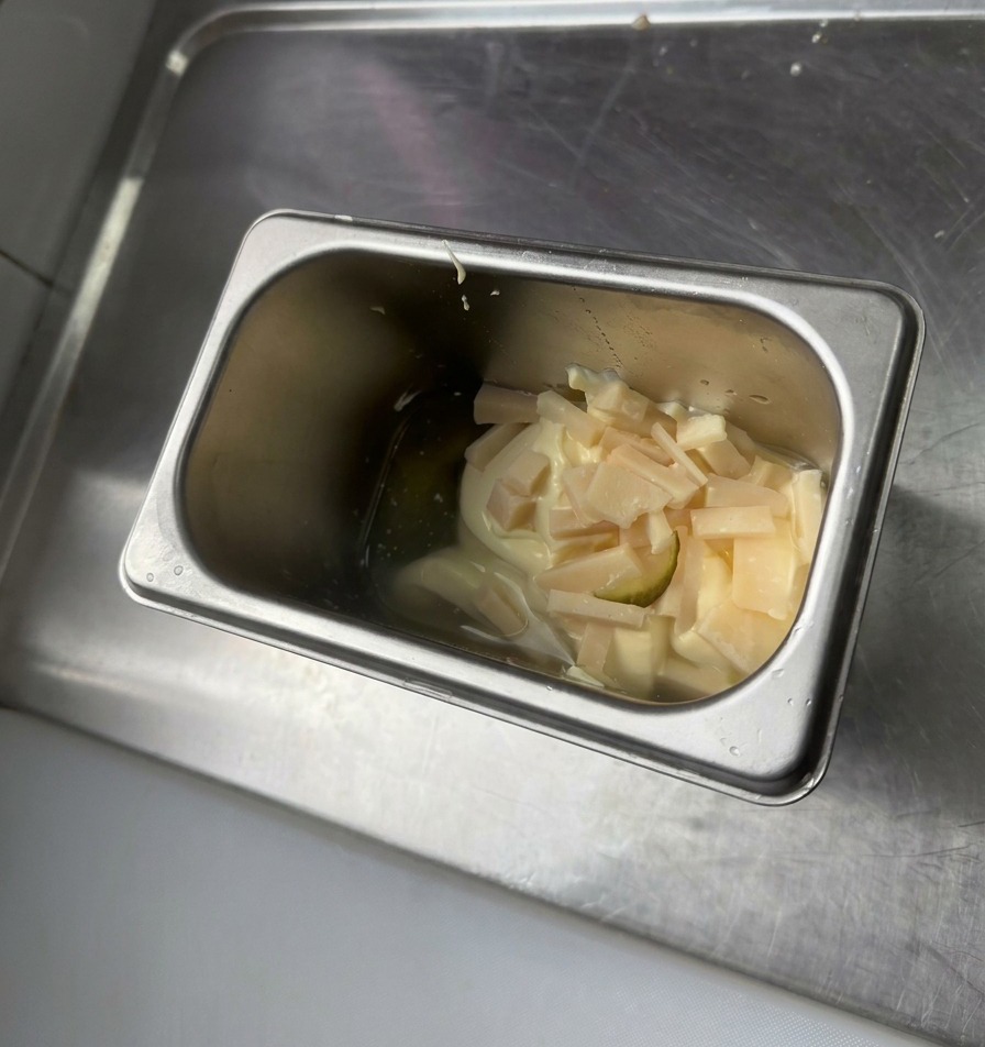 Un contenitore in acciaio inossidabile con maionese, senape gialla e piccoli pezzi di cetriolini tritati.