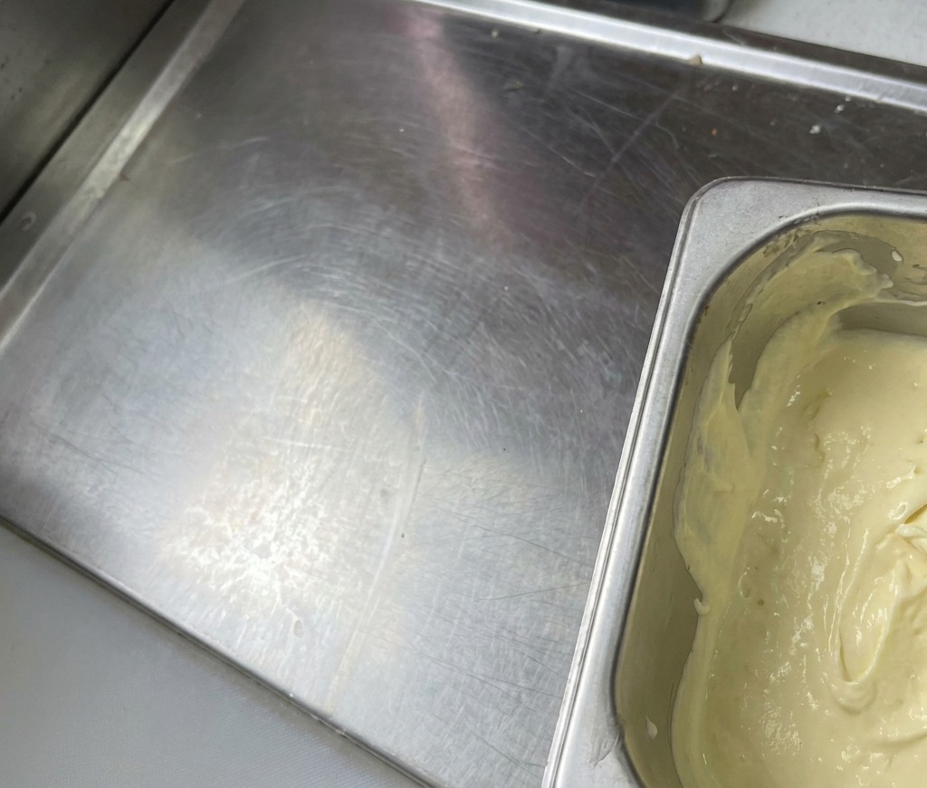 Un contenitore di metallo riempito con una salsa liscia, cremosa e di un colore giallo pallido.