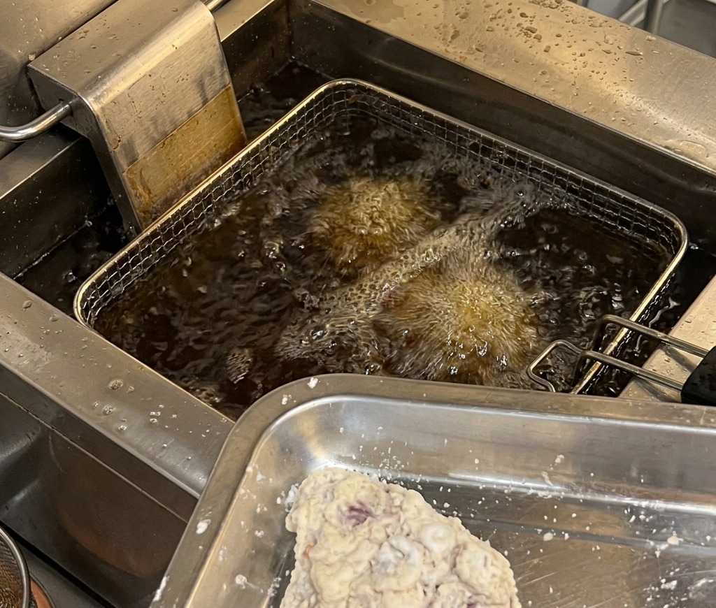 Pezzi di pollo impanati su un vassoio pronti per essere immersi in una friggitrice con olio caldo e bollente.
