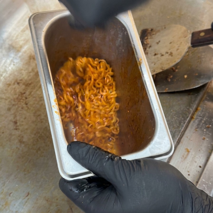 Noodle piccanti di colore rosso intenso mescolati allinterno di un contenitore profondo in acciaio inossidabile.