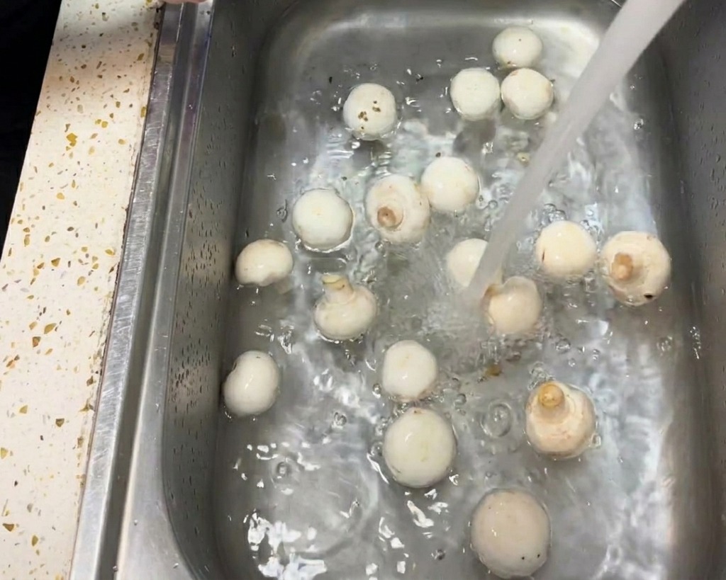 Un primo piano di una mano che usa un panno di carta inumidito per pulire delicatamente la cappella di un fungo champignon bianco.