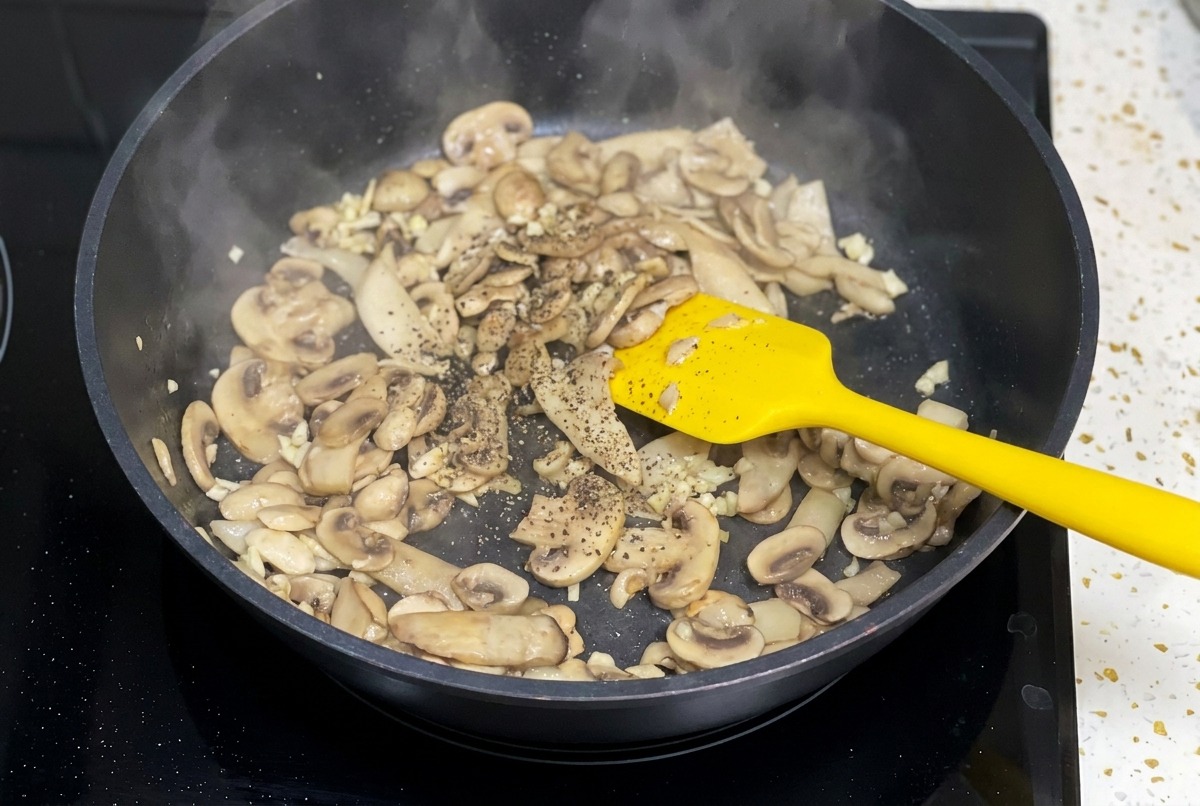 Funghi saltati in una padella nera che vengono conditi con una spolverata di pepe nero macinato.