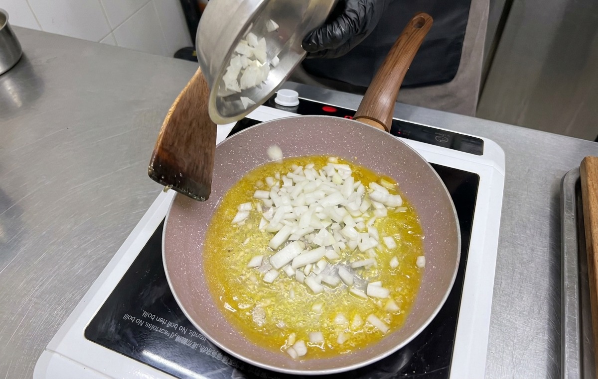 Cipolle bianche a dadini versate da una ciotola di metallo nella padella sopra laglio e il burro.