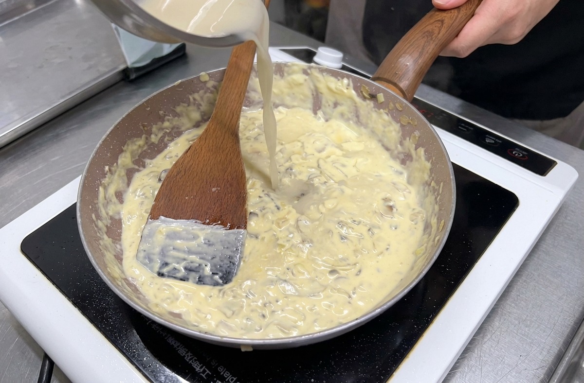 Brodo limpido versato da una ciotola in acciaio inossidabile in una padella di funghi e panna che sobbolle.