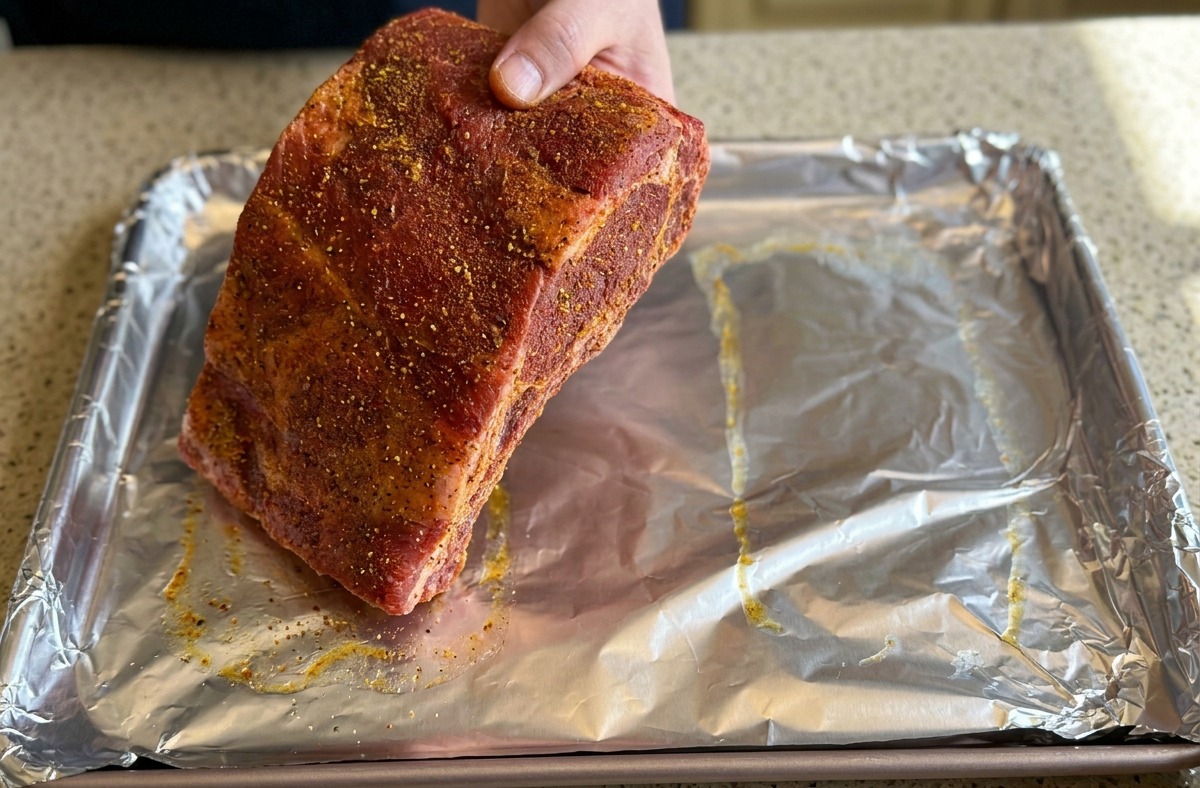 Una mano adagia un grande pezzo di costine marinate su una teglia da forno rivestita di foglio di alluminio.