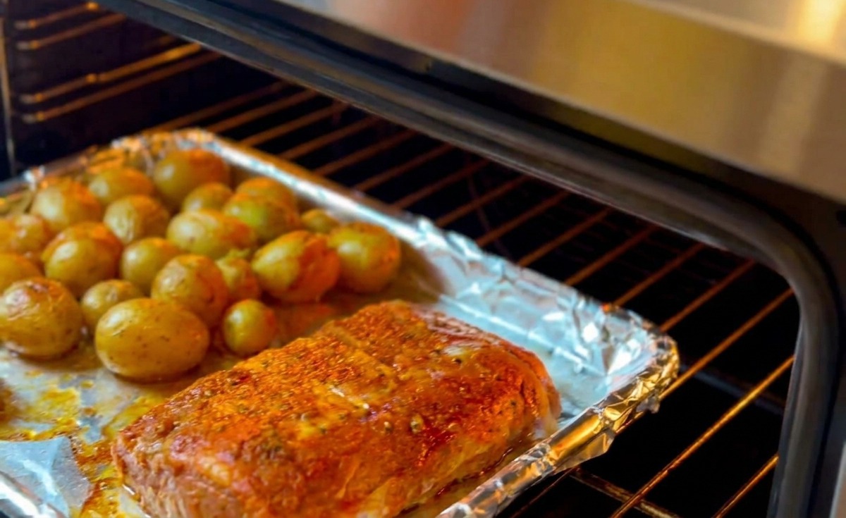 Una teglia con costine speziate alle erbe e patate novelle viene inserita in un forno preriscaldato per la cottura.