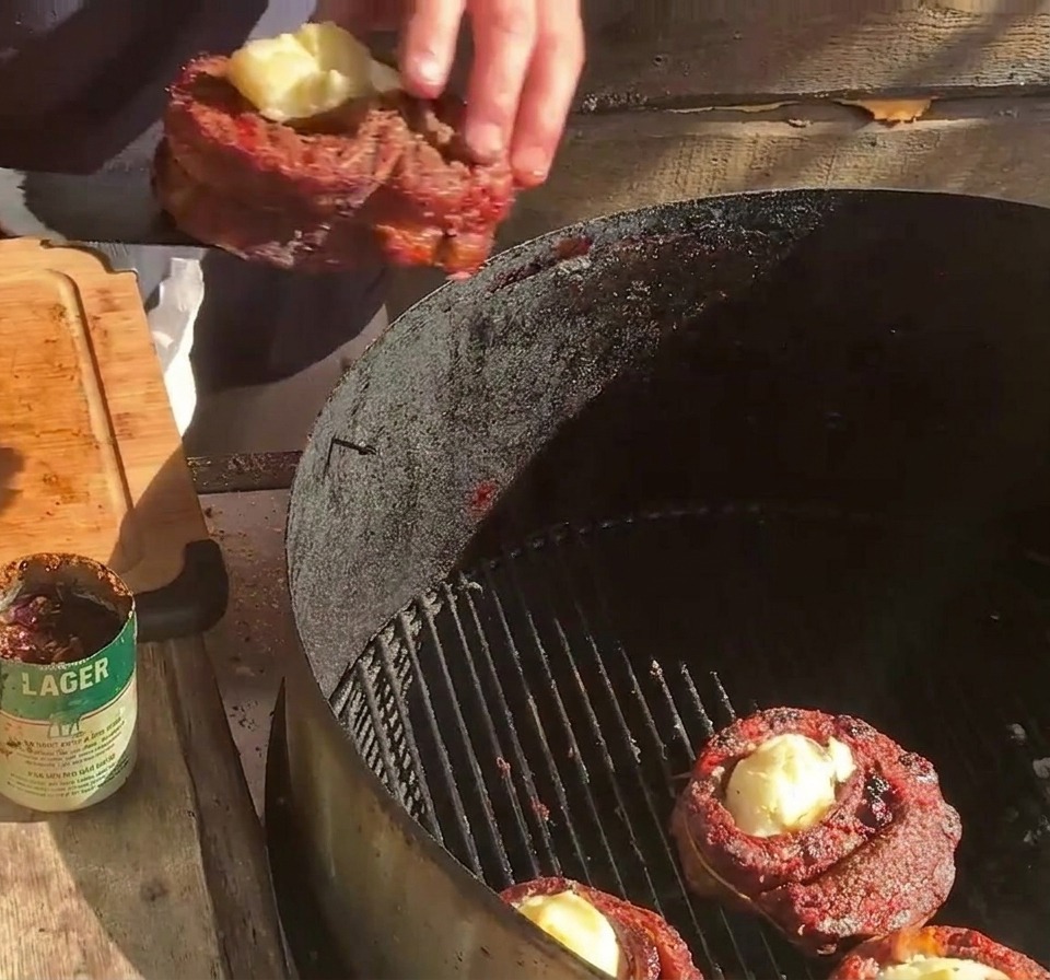 Una persona posiziona un cestino di costine farcito sulla griglia del barbecue accanto ad altri cestini e strisce di bacon.
