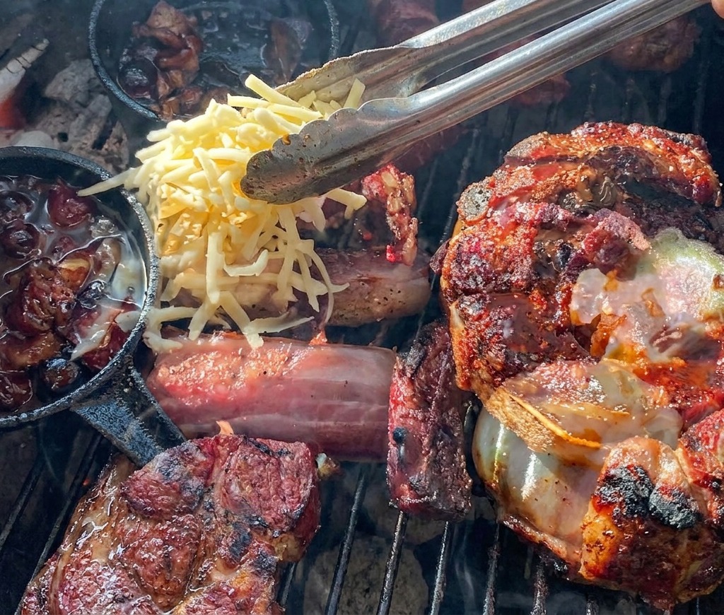 Pinze che fanno cadere formaggio giallo e bianco grattugiato su un cestino di carne grigliata farcito con una patata e salsa ai mirtilli.