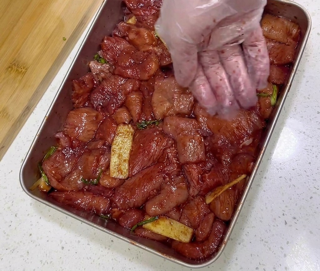 Fette di maiale rosso marinato in un vassoio dacciaio condite con un cucchiaio di fiocchi di peperoncino rosso.