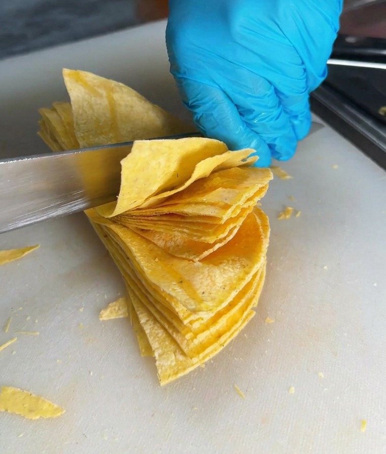 Un coltello affilato taglia una pila di tortillas di mais su un tagliere bianco per creare dei triangoli.