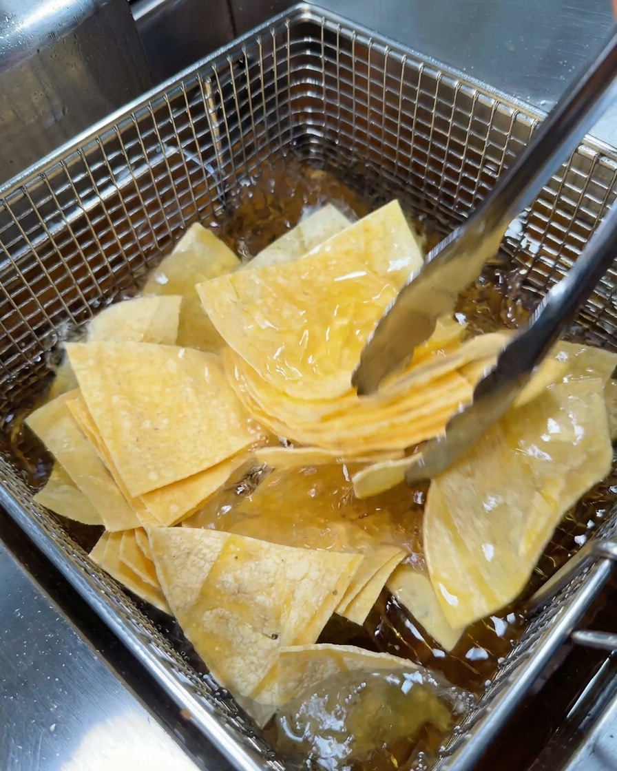 Pinze di metallo che posizionano una manciata di triangoli di tortilla nel cestello a rete di una friggitrice.