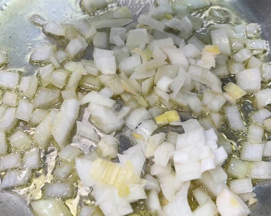 Cubetti di cipolla bianca che sfrigolano nellolio caldo in una padella.