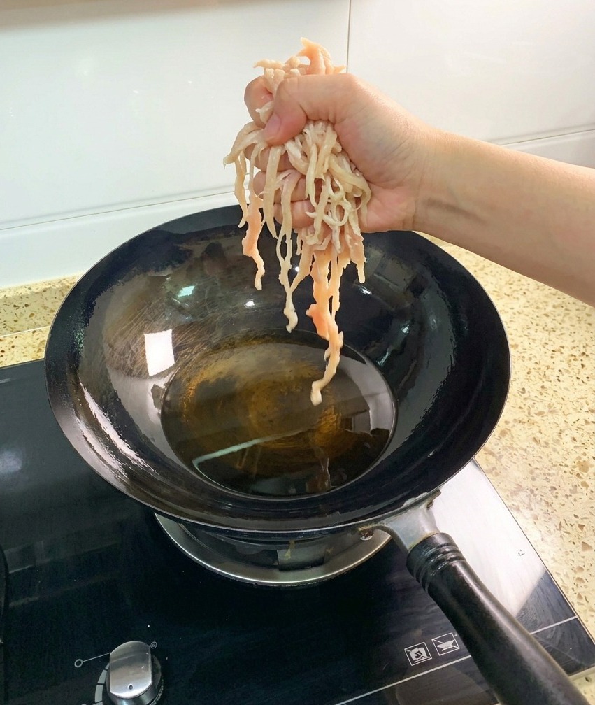 Mani che adagiano straccetti di petto di pollo crudo in un wok ben caldo con olio di semi limpido.