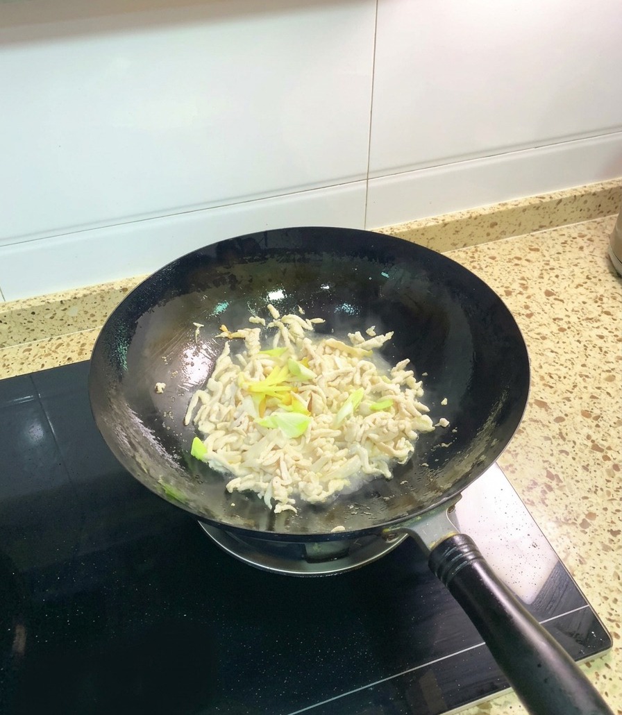 Straccetti di pollo parzialmente cotti che vengono saltati nel wok insieme a rondelle di cipollotto e fettine di zenzero fresco.