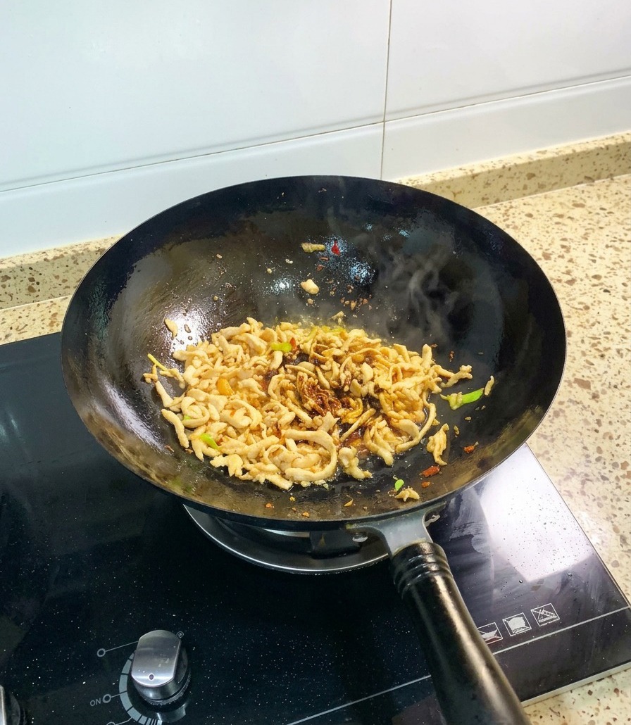Pollo sfilacciato che cuoce nel wok con la salsa di soia e laggiunta ben visibile della densa salsa dostrica.