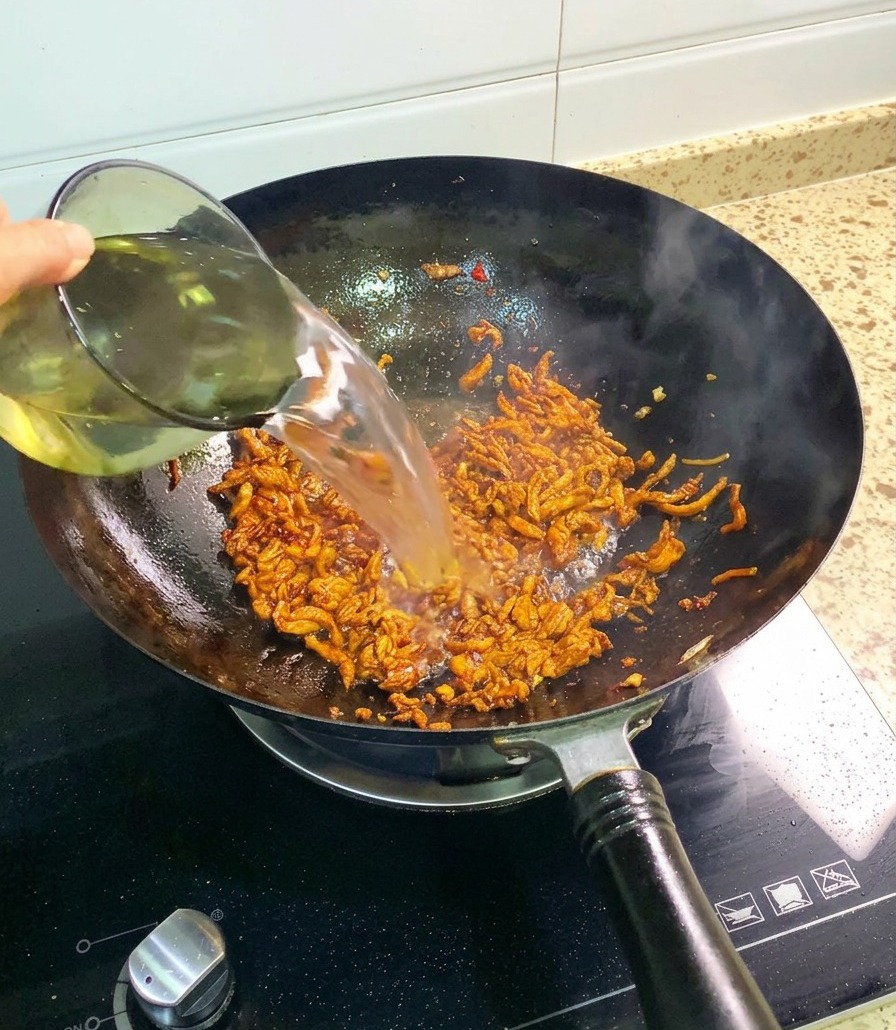 Un flusso dacqua limpida versato da un bicchiere di vetro allinterno del wok contenente il pollo già insaporito.