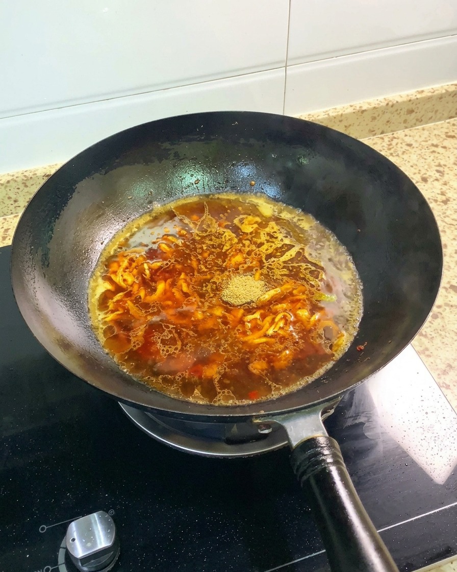 La polvere cinque spezie e un intero anice stellato adagiati sulla superficie del brodo rossastro nel wok.