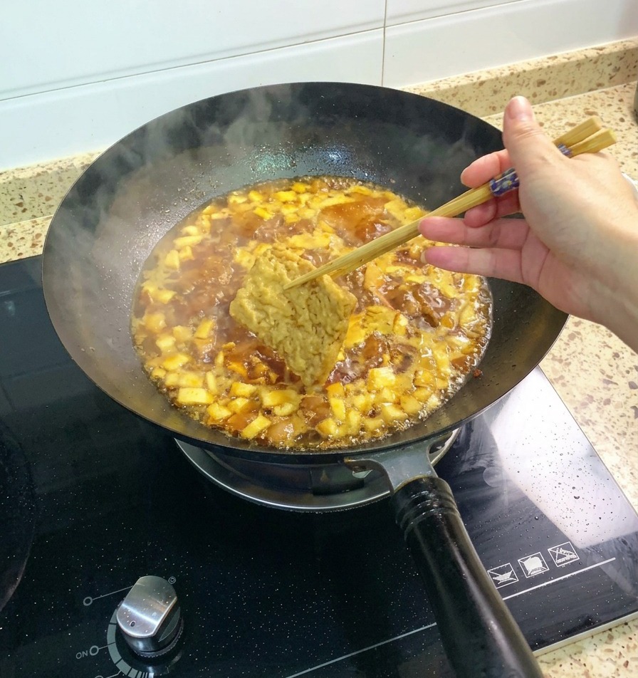 Una fetta di tofu fritto afferrata con le bacchette e immersa nel sugo di pollo e funghi che bolle allegramente.