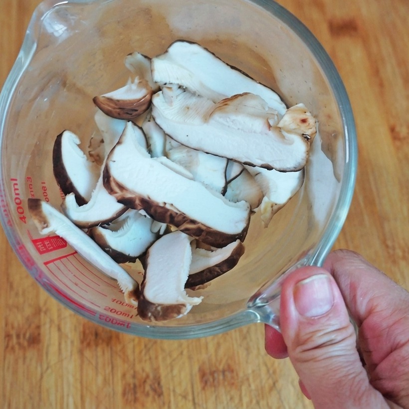 Una vista dallalto di funghi shiitake freschi affettati posti in un misurino di vetro trasparente su una base di legno.