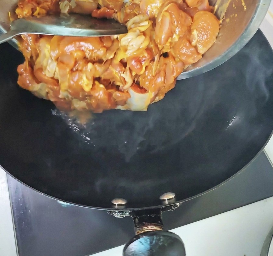 I pezzi di pollo marinato vengono versati da una ciotola metallica direttamente nel wok molto caldo che sprigiona vapore.
