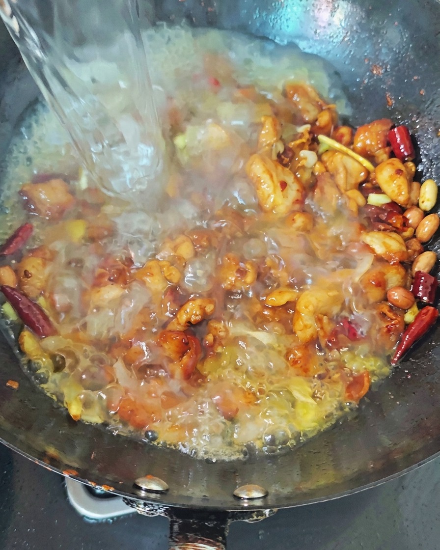 Acqua caldissima che viene travasata a filo nel wok sopra al pollo saltato e al peperoncino rosso per dar vita ad un brodo che borbotta animatamente.