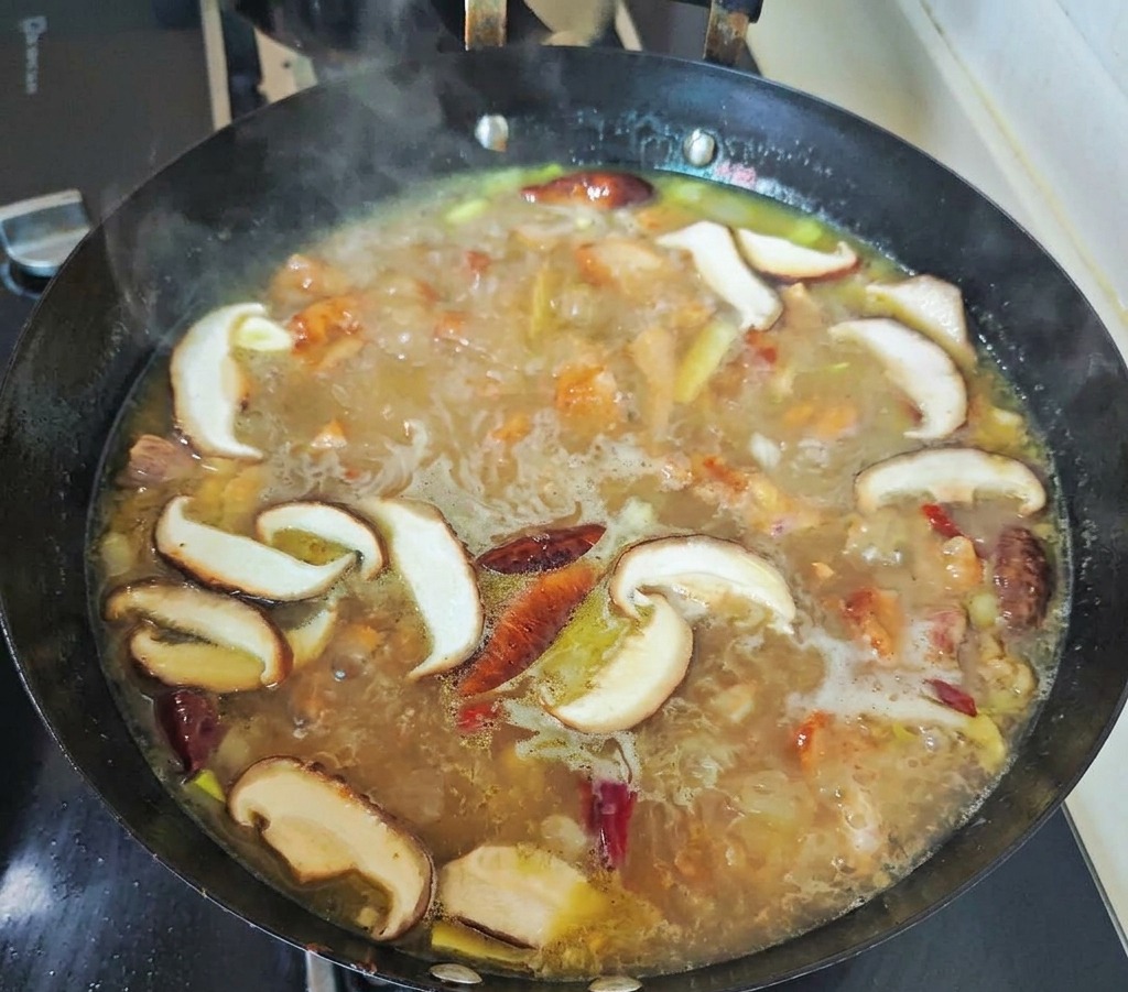 Il brodo dalle tonalità dorate che sobbolle lentamente dentro un grosso tegame nero assieme ai funghi shiitake appena tagliati e ai peperoncini rossi interi.
