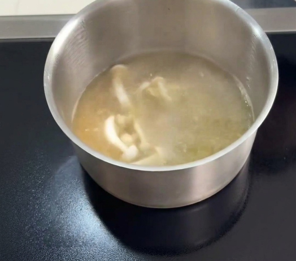 Funghi white jade e sottili filamenti arancioni di fiori di cordyceps vengono aggiunti a una pentola di brodo limpido di pollo in ebollizione.