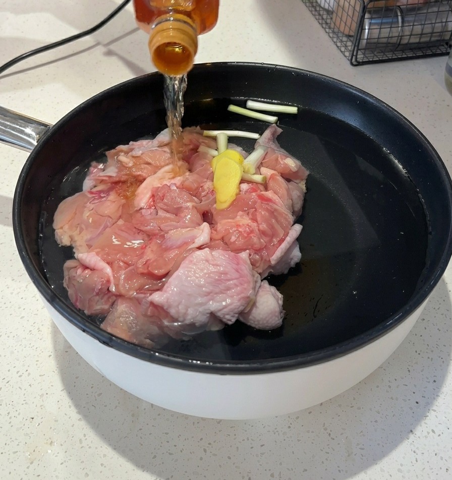 Versare un liquido ambrato limpido da una bottiglia di vetro nella pentola con acqua e pollo.