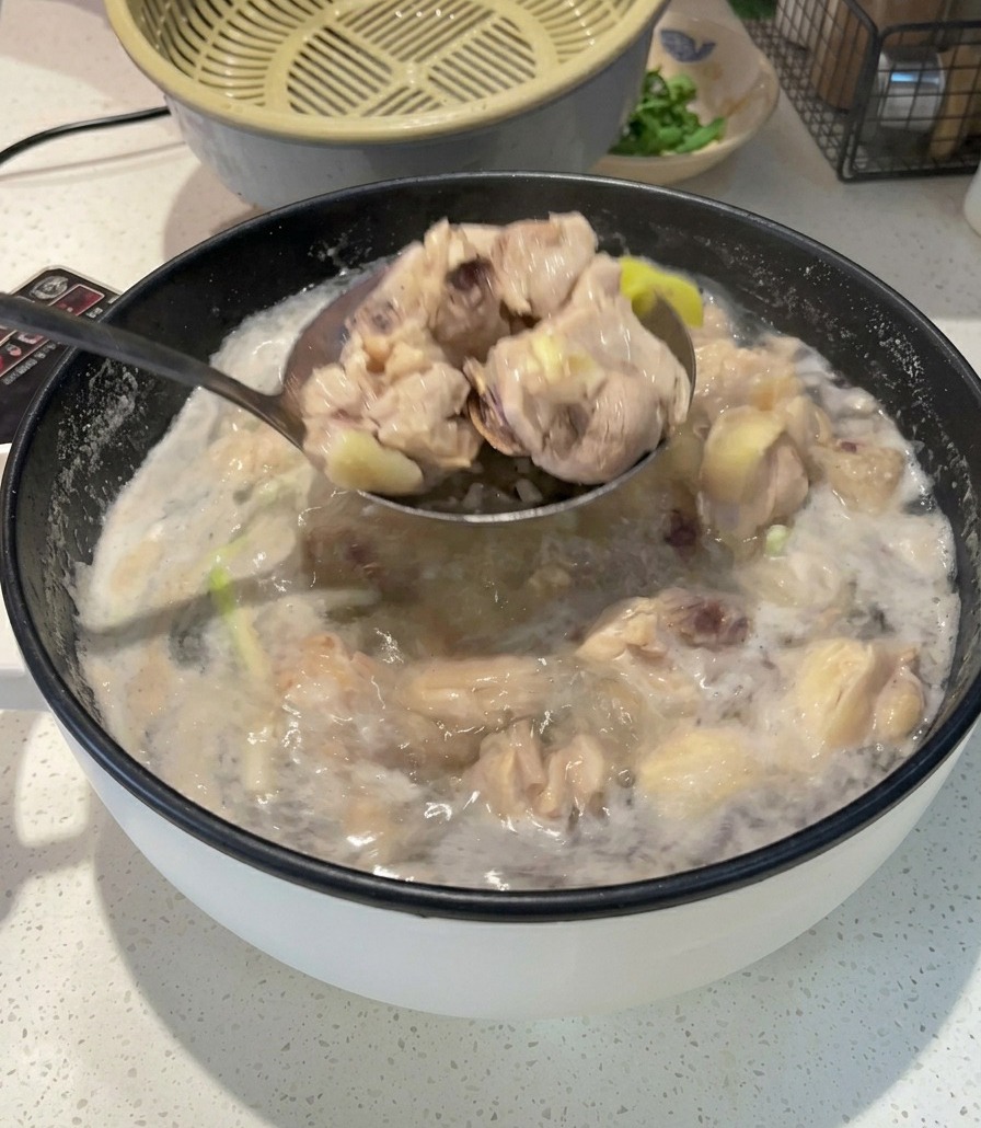 Un mestolo di metallo che solleva pezzi di pollo opachi e sbollentati da una pentola di acqua bollente e schiumosa.