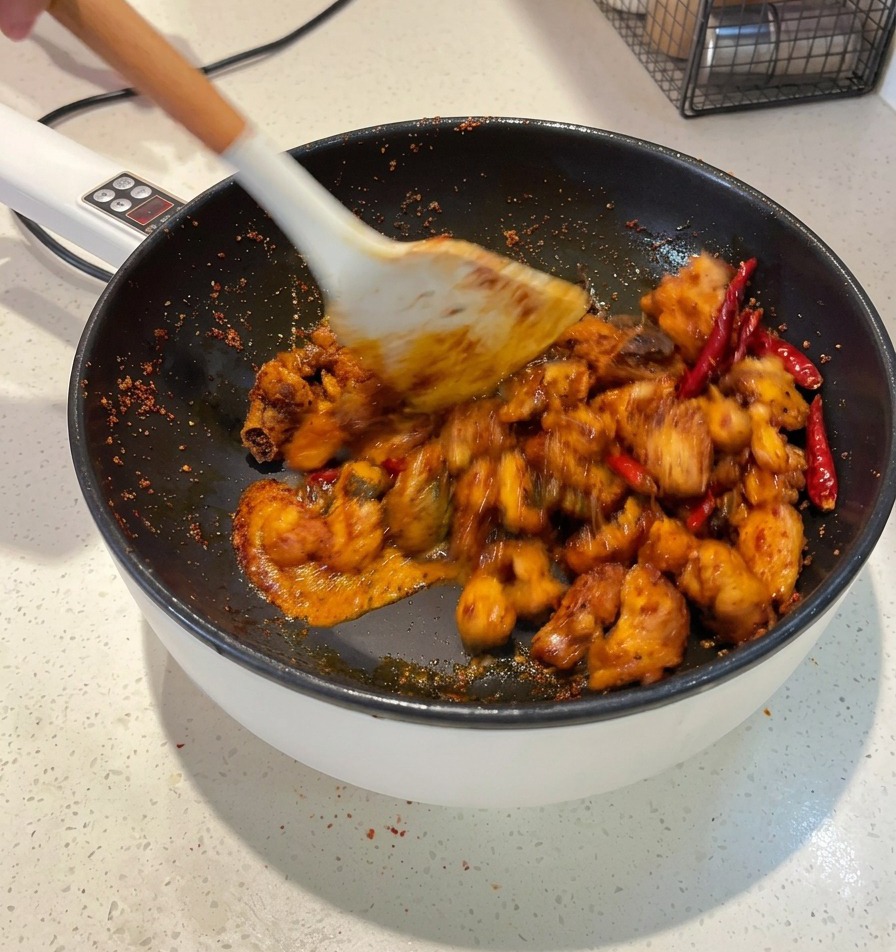 Una spatola bianca che salta pezzi di pollo in una salsa rosso scuro allinterno di una padella finché ogni pezzo non è rivestito.