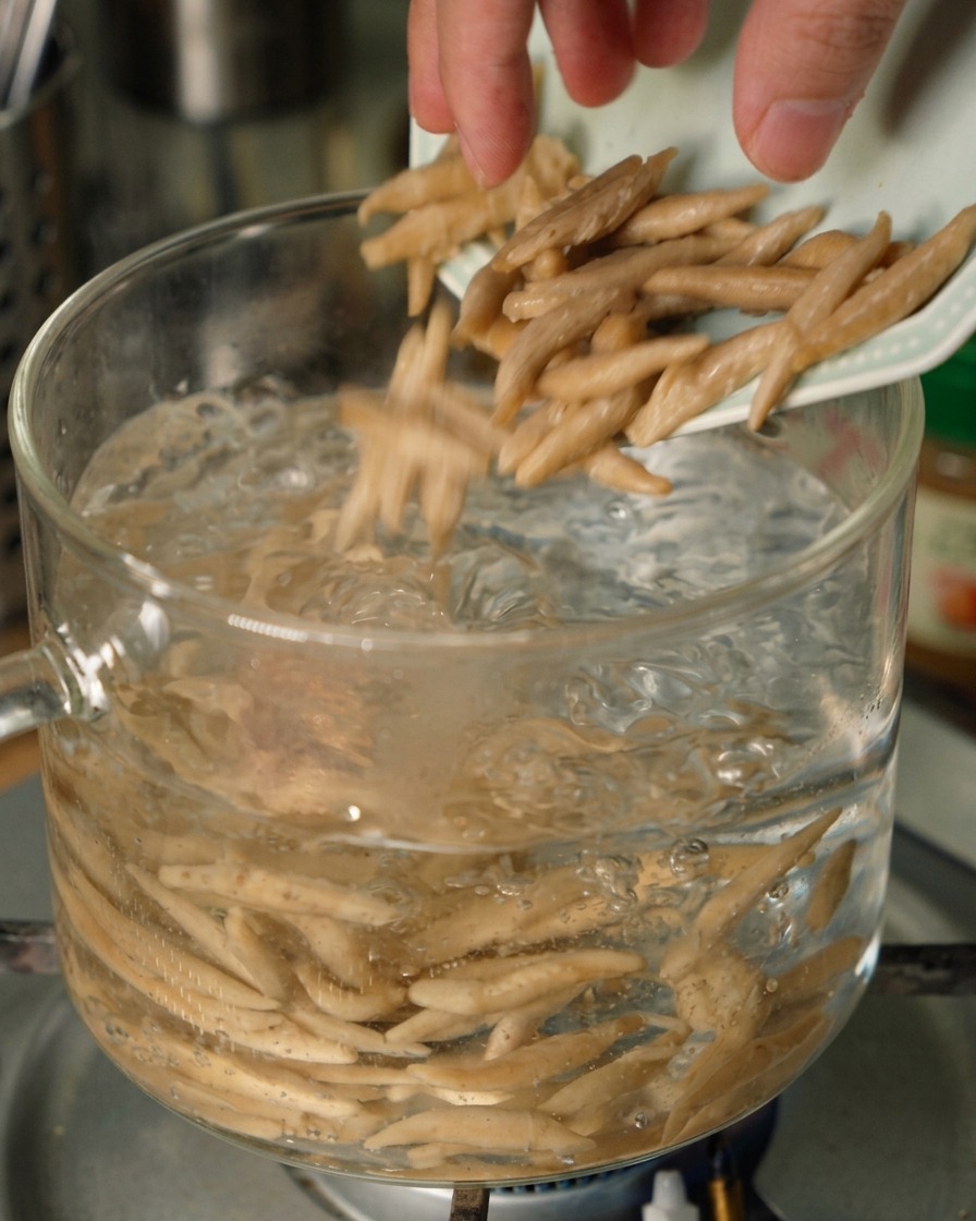 Noodles davena sottili cadono da un piattino in una pentola di vetro trasparente con acqua che bolle visibilmente.