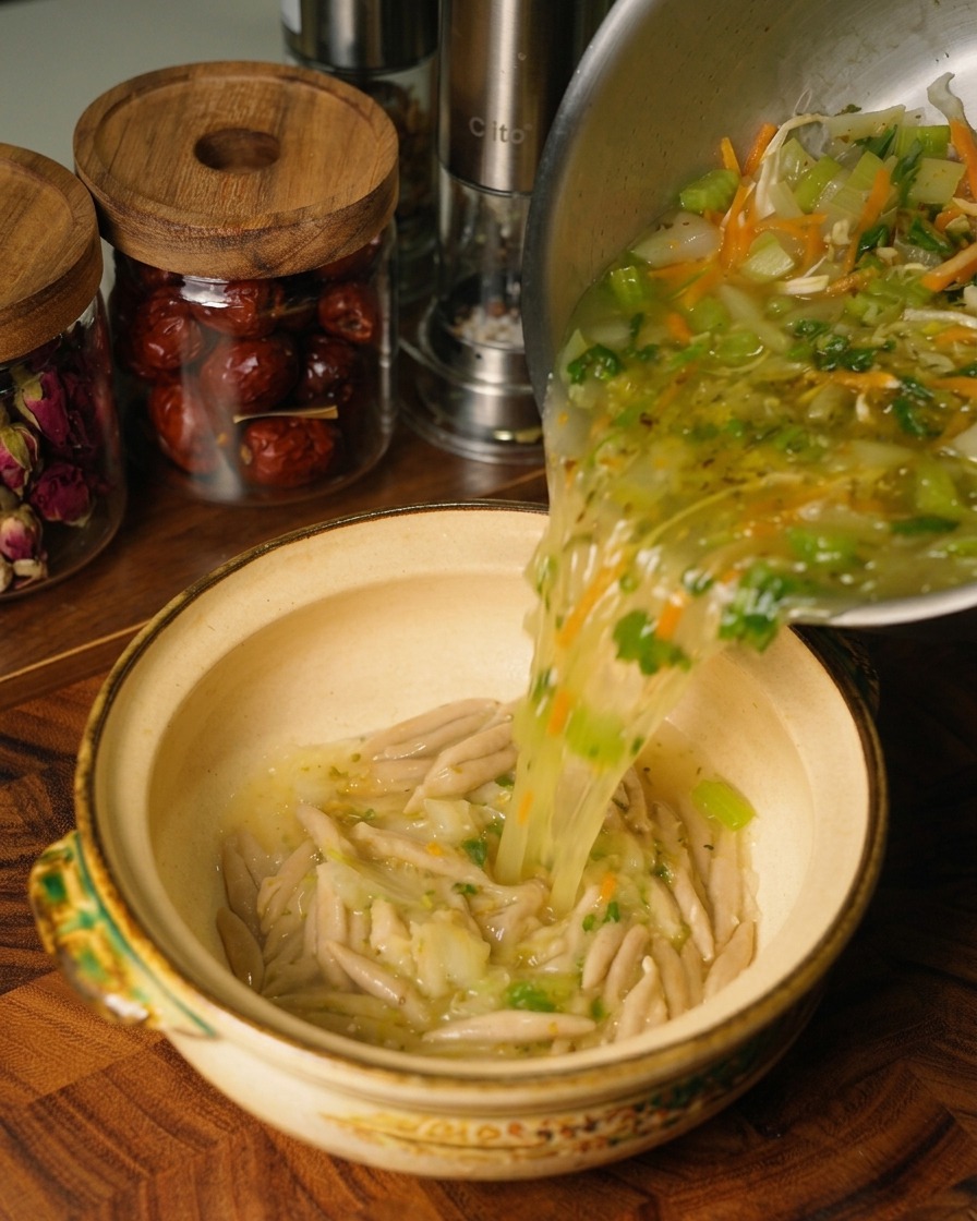 Zuppa calda di pollo e verdure viene versata da una pentola dacciaio in una ciotola di ceramica contenente i noodles davena cotti.