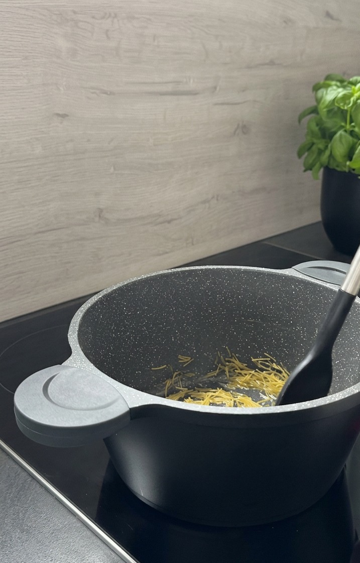 Pastina tipo risoni mescolata con una spatola nera in una pentola grigia effetto granito mentre tosta fino a diventare dorata.