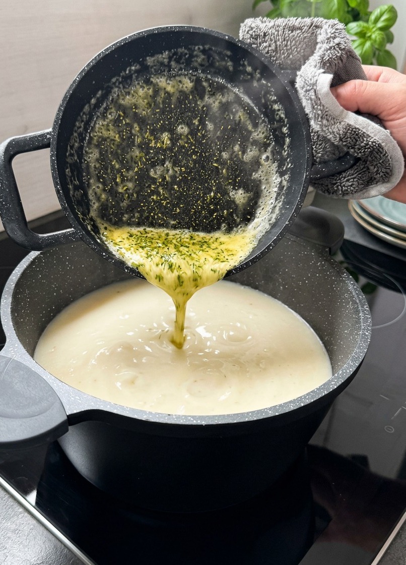 Burro giallo fuso con foglioline di menta essiccata versato da un pentolino nero direttamente nella zuppa cremosa.